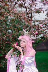 Deer dryad girl against the background of a blooming pink apple tree