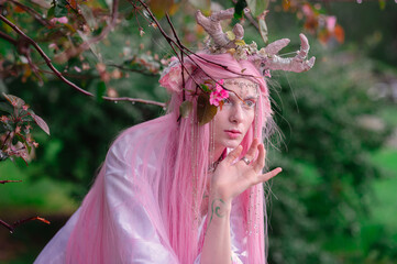Deer dryad girl against the background of a blooming pink apple tree
