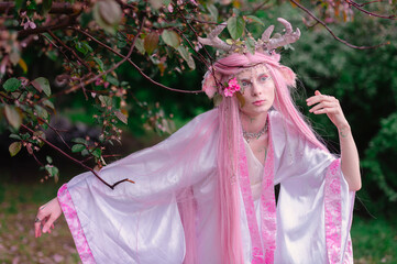 Fototapeta premium Deer dryad girl against the background of a blooming pink apple tree