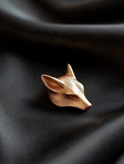 Elegant fox head brooch in a warm gold tone resting on a rich, dark fabric backdrop. Timeless accessory.