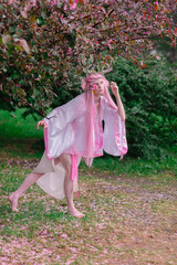 Deer dryad girl against the background of a blooming pink apple tree