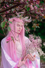 Deer dryad girl against the background of a blooming pink apple tree