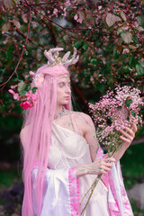 Deer dryad girl against the background of a blooming pink apple tree