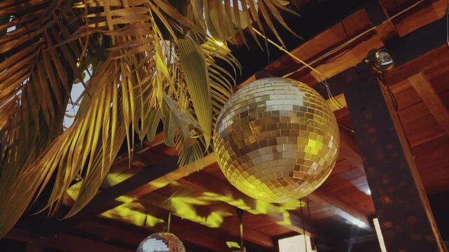 Camera smoothly moves around a golden disco ball, reflecting light and creating a sparkling, festive atmosphere in a dark party setting