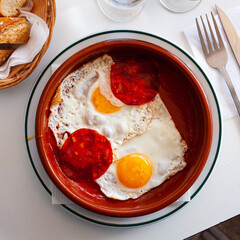 Fried sunny-side-up eggs with sausage and tomatoes in bowl..
