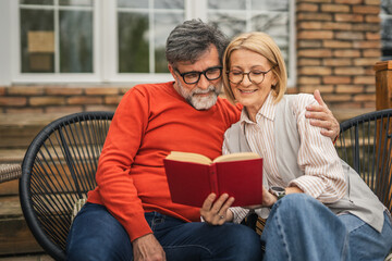 aged couple sit in front house and read book spent time together