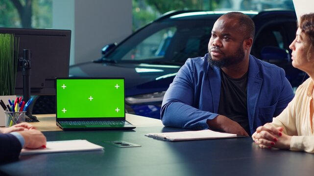 Dealership salesman showing car models on isolated screen laptop to clients, making recommendations. Showroom agent presents financing options to customers on mockup notebook, camera A