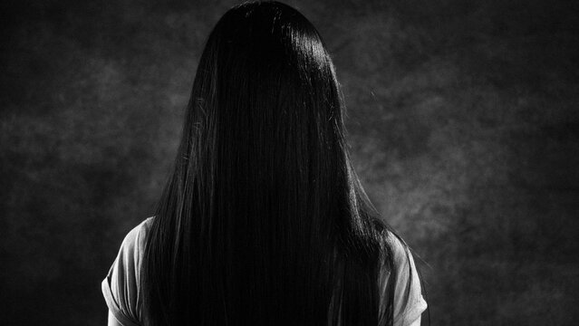 Black and white portrait of a woman with long black hair covering her face, creating a mysterious and anonymous atmosphere
