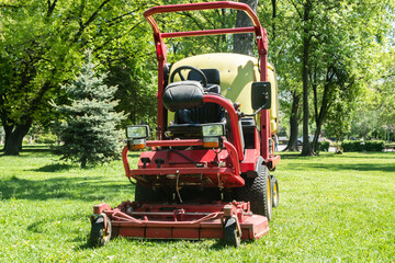 Professional multifunctional ride on lawn mower on green grass in city park in spring time