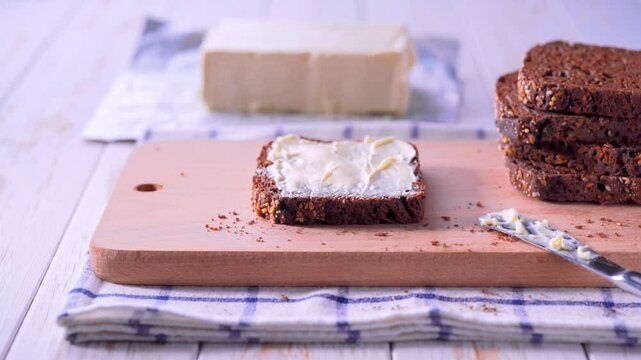 Tasty cut multigrain sourdough bread with fresh butter on a white wooden table. Sliced rye bread with butter on a white wooden table, selective focus.
