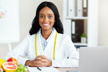 Portrait of professional black dietitian smiling at camera in weight loss clinic. Millennial...