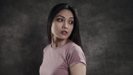 Woman in pink shirt looking sideways against dark background
