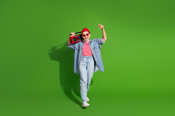 Trendy woman in casual denim outfit holding a boombox on a lively green background, showcasing retro style and positive vibes