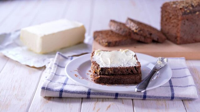 Sliced rye bread with butter on a white wooden table, selective focus.  Tasty cut multigrain sourdough bread with fresh butter on a white wooden table.