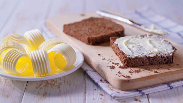 cut multigrain sourdough bread with fresh butter curls on a white wooden table. Sliced rye bread with butter curls on a white wooden table, selective focus.