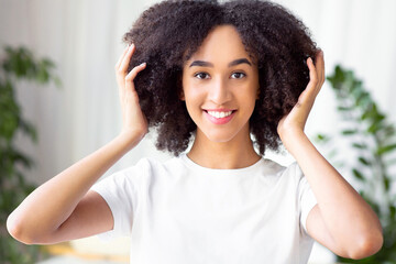 Fototapeta premium Perfect hairstyle, beautiful strands, cool look and new style. Laughing cute millennial african american female touches curly healthy hair in interior of bathroom and enjoying haircut, free space