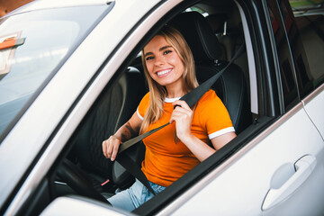 Naklejka premium Woman fastening seatbelt in car interior showing safe driving practices and cheerful mood during a sunny urban commute