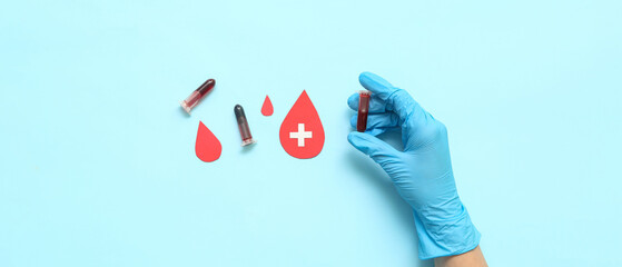 Female doctor with test tubes and paper blood drops on blue background. World Donor Day