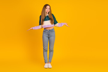 Trendy young woman with relaxed gestures posing against a vibrant yellow background, showcasing a stylish pullover and jeans outfit