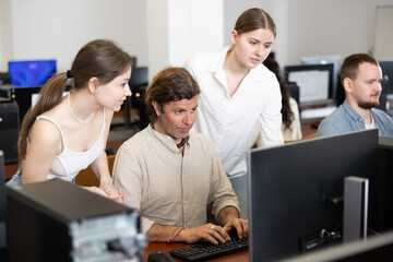 Fototapeta premium Adult man and two young women colleagues discussing work at computer in office