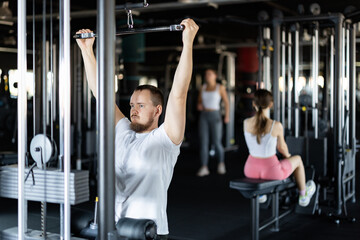 Young athletic man in sportswear training his arms muscles on machine in gym