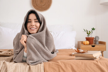 Beautiful young happy woman with warm plaid lying in bedroom at home