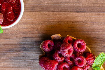Spoon with raspberry and bowl with raspberry jam on wooden background
