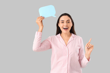 Young woman in striped pajamas with blank speech bubble pointing at something on light background
