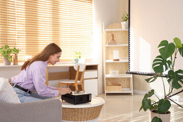 Young woman with modern projector on coffee table in stylish living room
