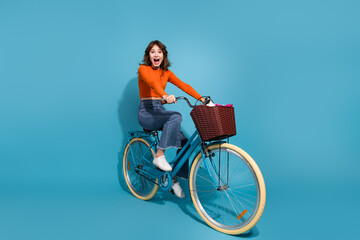 Cheerful young woman riding a bright blue bicycle in a stylish orange outfit enjoying a fun and...