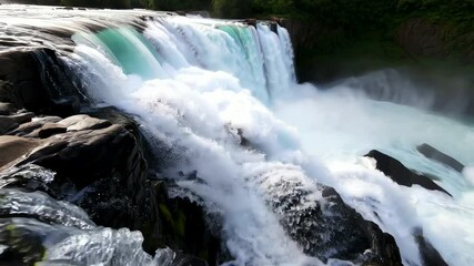 A wide view of a strong waterfall cascading over dark rocks with mist rising, representing the power of nature, suitable for nature documentaries or travel vlogs showcasing natural wonders