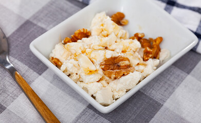 Portion of appetizing farm cottage cheese with walnuts and honey poured on top