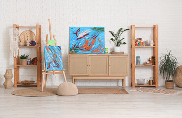 Interior of artist's workshop with paintings, commode and art supplies on shelving units