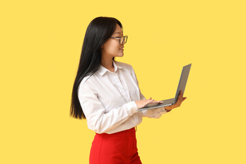Beautiful young Asian woman working with modern laptop on yellow background
