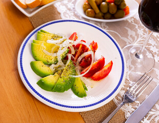 Fresh tomato and avocado divided in pieces and onion rings served in a plate with necessary table laying