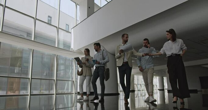 A diverse business team walks and talks in a modern, spacious office, discussing projects and strategies. Collaboration and professionalism are evident.