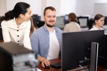 Female teacher helps man with learning on computer in university computer class