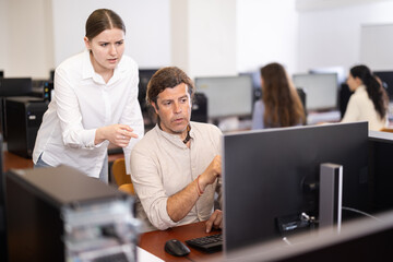 Obraz premium Female teacher helps man with learning on computer in university computer class