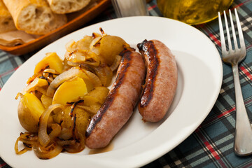 Tasty sausages being cooked on grill with vegetable garnish of baked potatoes and onion