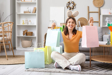 Young woman in bunny ears with shopping bags sitting at home on Easter Day