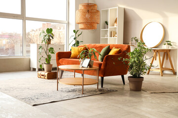 Interior of stylish living room with brown sofa, houseplants, coffee table and mirror