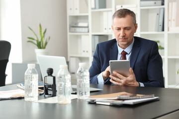 Fototapeta premium Portrait of handsome mature businessman working with tablet computer at table in office