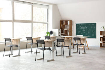 Interior of classroom with blackboard, shelf unit and desks. End of school year