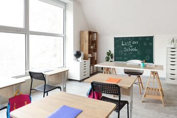 Interior of classroom with blackboard, shelf unit and desks. End of school year
