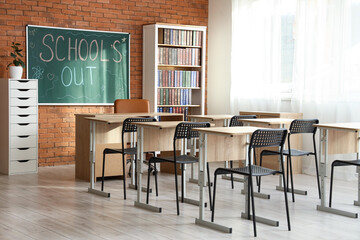 Blackboard with text SCHOOL'S OUT on brick wall in classroom interior