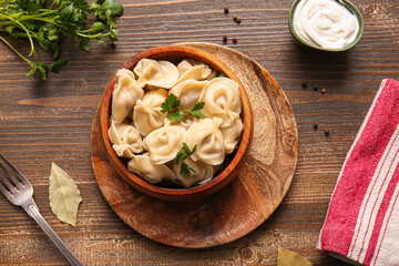 Bowl of delicious boiled dumplings with parsley and sour cream on wooden background