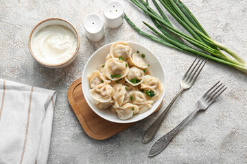 Bowl of delicious boiled dumplings with green onion and sour cream on grey background