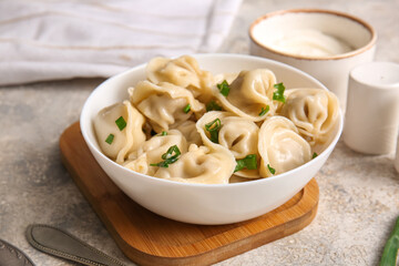 Bowl of delicious boiled dumplings with green onion and sour cream on grey background, closeup