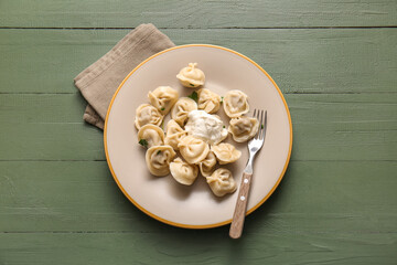 Plate of delicious boiled dumplings with sour cream and parsley on green wooden background