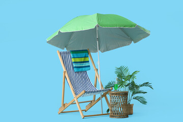 Striped deck chair with umbrella and wicker table on blue background